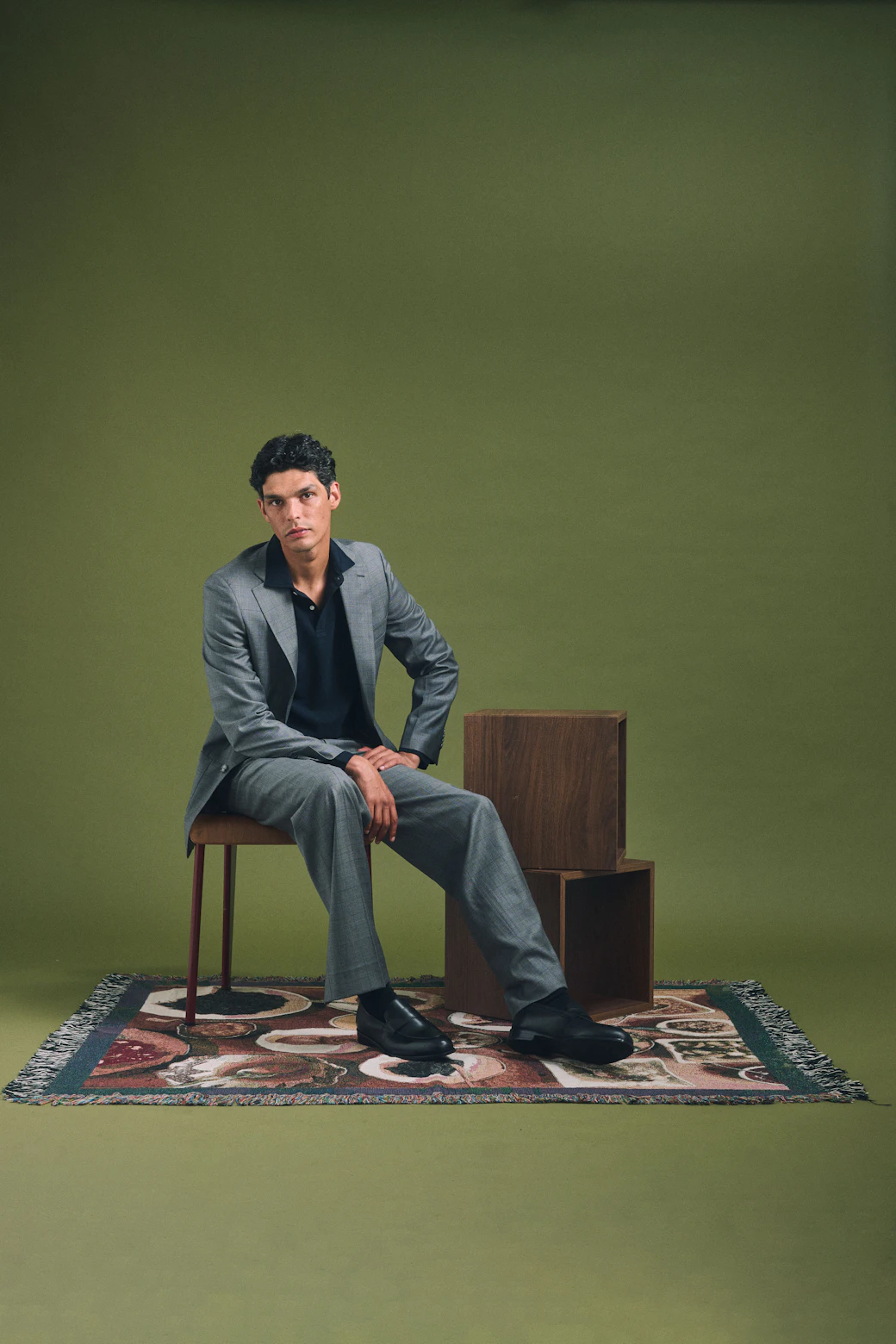 The Varallo Loro Piana charcoal glen plaid suit worn seated on a patterned rug