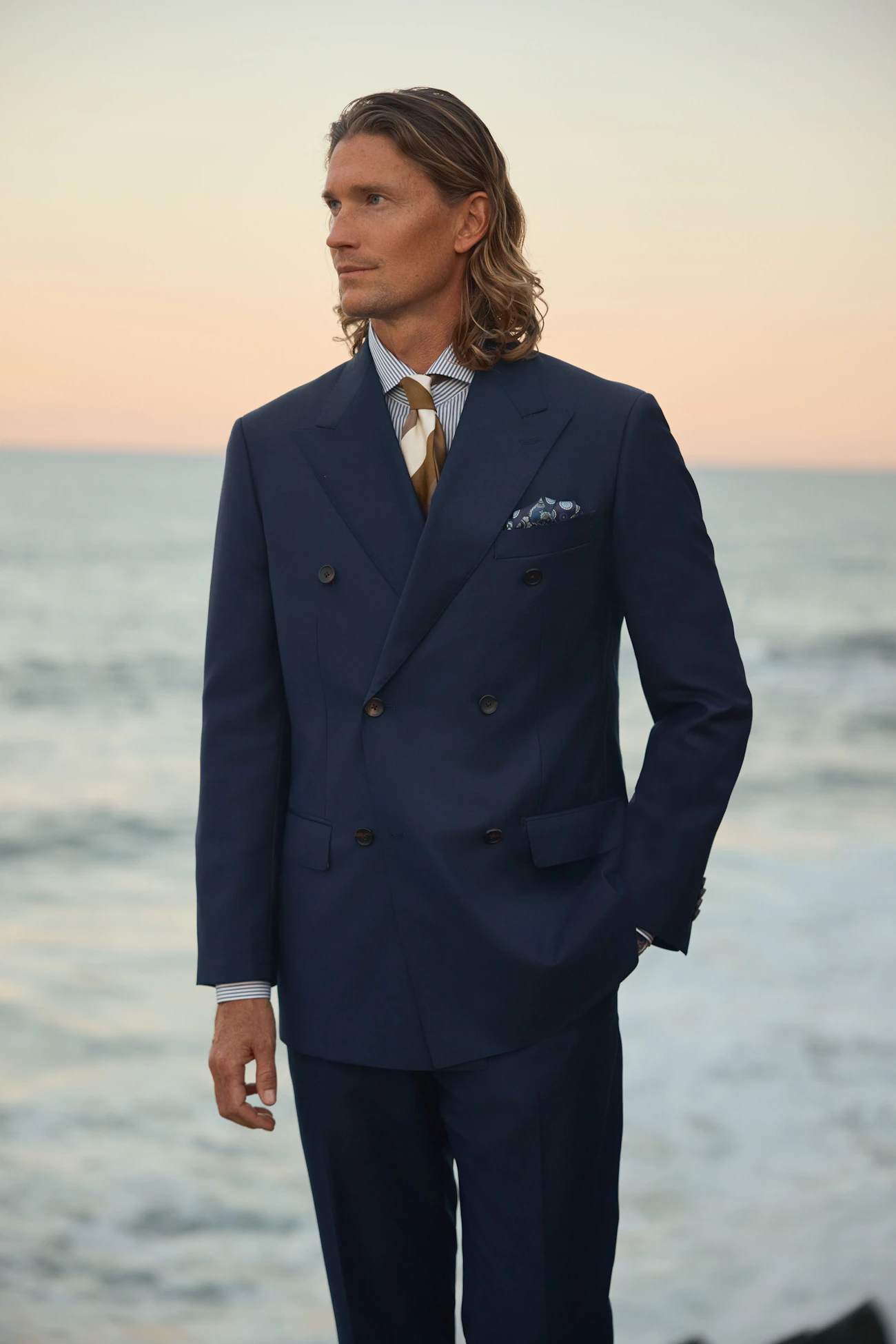 The Esperence navy wool suit, worn with a gold tie against the sea